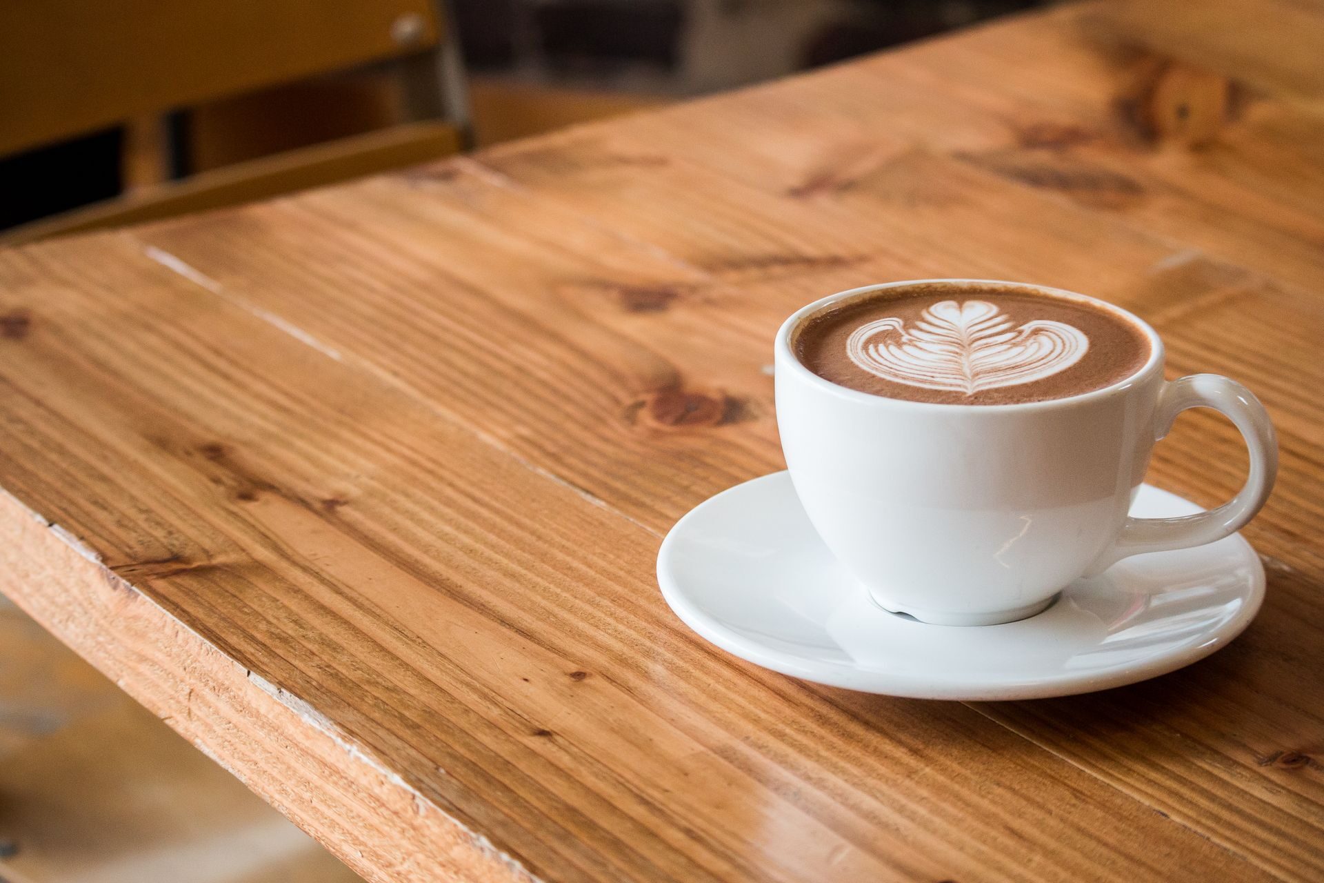 A white coffee cup with latte art on a saucer, photographed from the side on a wooden table